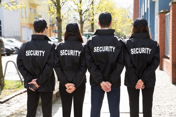 Four security guards standing with their backs to the camera, representing the ongoing need for human security teams.