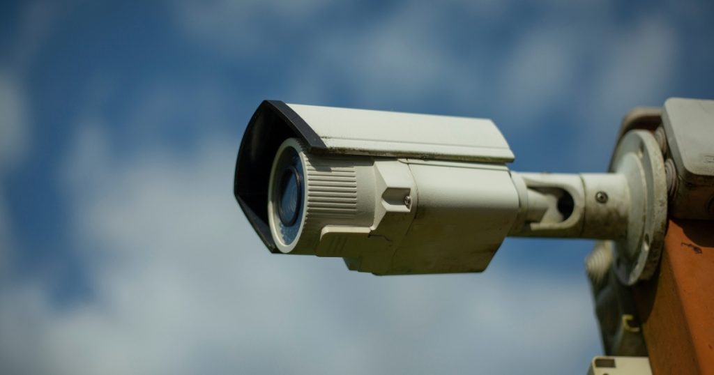 A white outdoor security camera against a blue sky, representing traditional fixed perimeter security systems.